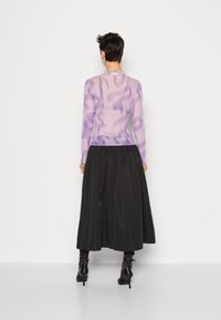 Durchsichtige langärmelige Bluse in Lavendel mit abstrakten Mustern; kombiniert mit einem schwarzen, fließenden, knöchellangen Rock und passenden schwarzen Absatzstiefeln.