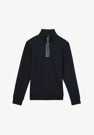 Merinopaita tummansinisellä värillä, korkea kaulus ja puolipitkä vetoketju, jossa on nahkavarustus. Sujuva pinta, jossa istuvat hihansuut ja helma.