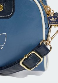 Blue leather bag corner with gold buckle, adjustable strap, white trim, and navy Adidas zipper pull with logo.