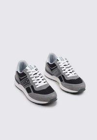 Zapatillas deportivas en tonos gris y negro, confeccionadas con materiales de malla y ante, que presentan un diseño con cordones blancos, un acento de logo y un cuello acolchado.