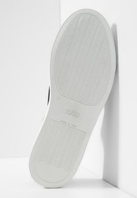 Semelle en caoutchouc blanche avec motif ondulé, arborant le logo embossé "HUGO" et le texte "MADE IN ITALY". Bord supérieur noir visible.