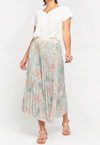 Floral patterned maxi skirt in light blue, featuring a wide elastic waistband. Paired with a white short-sleeve top and gold sandals.