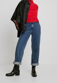 Schwarze Lederjacke über einem roten Strickpullover, kombiniert mit hoch taillierten blauen Jeans, die an den Bündchen hochgerollt sind, und schwarzen Ankle Boots mit Blockabsatz.
