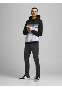 Zwarte en grijze hoodie met een logo aan de voorkant, gecombineerd met cargobroeken in een donkere kleur. Model staat op sportieve schoenen. Eenvoudig, modern ontwerp.