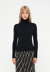 Suéter negro de cuello vuelto con mangas largas, hecho de un material de punto suave. Diseño ajustado que se extiende hasta las caderas, combinado con una falda de estampado.