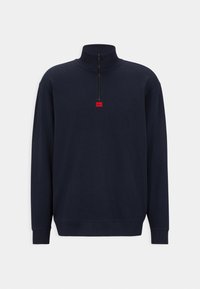 Felpa blu navy con colletto alto, collo con zip e una piccola etichetta rossa sul petto. Tessuto morbido e polsini a costine.