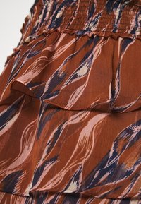 Tejido con un patrón marrón y rosa, con un cuerpo fruncido y capas con volantes, presentando diseños fluidos en forma de olas en azul oscuro y acentos en crema.