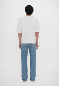 Hvit bomulls t-skjorte med korte ermer, vist fra baksiden. Kombinert med lyseblå denimjeans, rett ben design, og minimal detaljer.