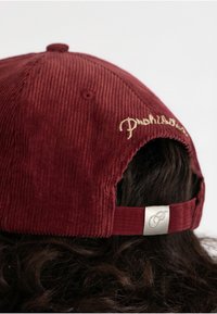 Burgundia kašmiri müts hõbedase metallregulaatori ja kuldse brodeeritud tekstiga taga. Pehme tekstuur ja struktureeritud disain.