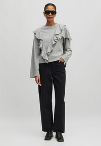 Graues Langarmoberteil mit asymmetrischen Rüschendetails vorne, kombiniert mit schwarzen geraden Hosen und schwarzen Ankle Boots.