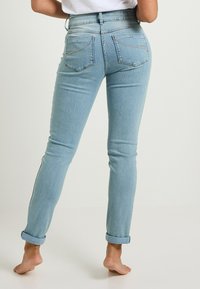 Jeans de cintura alta en azul claro, con una silueta ajustada, puños enrollados, bolsillos traseros y detalles de costura sutiles. Textura de denimb suave.