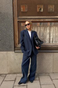 Blazer azul marino de corte grande y pantalones de pierna ancha, combinados con una camisa blanca, bolso negro y gafas de sol. Tejido suave con un detalle mínimo.