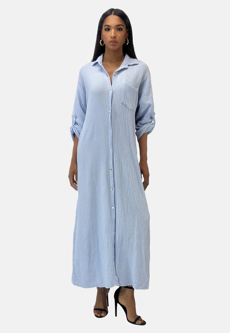 Button-up, long, blue striped dress with a textured fabric, roll-up sleeves, and front pocket; worn with black high-heeled shoes.