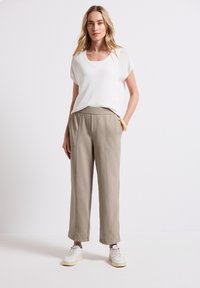 Lätt vit topp med rundad halsringning, kombinerad med beige vida byxor med framfickor och en slät textur. Vita sneakers.