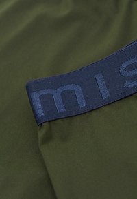 Olivgrön tyg med en matt yta som har ett mörkblått elastiskt band. Bandet har broderad text i ljusblått.