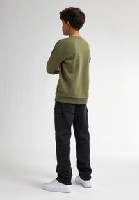 Olijfgroen sweatshirt met lange mouwen en ribgebreide manchetten, gecombineerd met zwarte cargobroek met zakken en witte sneakers.