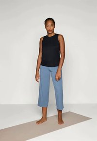 Svart ermeless topp, lyseblå vide bukser, mykt stoff, glatt tekstur, uten mønstre, barføtt på en lys yogamatte.