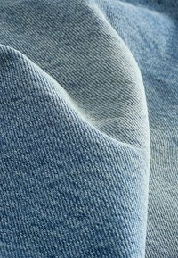 Țesătură de denim de culoare albastru deschis, cu o textură moale, având un model de țesătură subtil și o suprafață netedă. Două straturi sunt așezate unul peste celălalt.