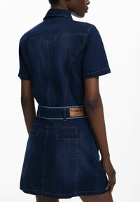 Denim haljina s kratkim rukavima, tamnoplavih boja, uskog struka, raširenog suknje, s brendiranim oznakom na leđima i dvostrukim džepovima.