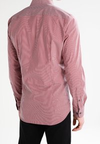 Chemise à rayures rouges et blanches à manches longues avec un col button-down, dotée de boutons noirs et d'un ourlet arrondi. Tissu lisse et léger.