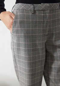 Grå rutiga byxor i ett strukturerat tyg med svarta, vita och subtila röda linjer, sidofickor och en skräddarsydd passform.