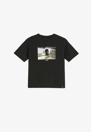 Czarna koszulka z grafiką wysokiej, szczupłej czarnej postaci stojącej w słabo oświetlonym parkingu z żółtymi oznaczeniami.