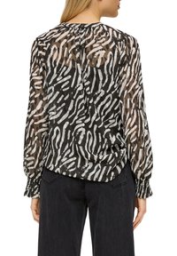 Blusa a righe zebrate bianco e nero trasparente con maniche lunghe, polsini arricciati e leggero arricciamento sul retro. Tessuto testurizzato.
