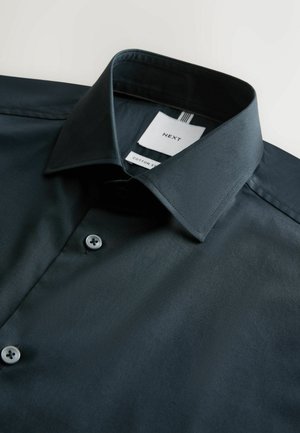 Mørkegrøn bomuldsskjorte med en klassisk krave, der har én knaplukning og et mærke med mærkedetaljer. Glat tekstur.