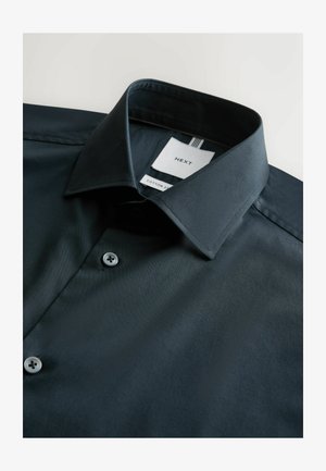 Tumeheles roheline puuvillane särk klassikalise kraega, millel on ühe nupuga kinnis ja kaubamärgi detailidega silt. Sile tekstuur.