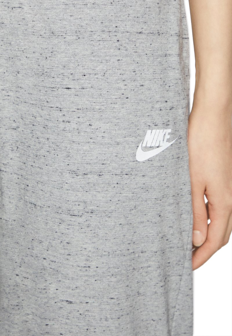 Zbliżenie szarego materiału Nike w plamki z białym logo i częścią ręki osoby spoczywającej obok niego.