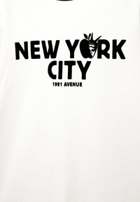 Hvid bomulds t-shirt med fed sort tekst: "NEW YORK CITY" og "1991 AVENUE," med et grafisk billede af Frihedsgudinden i stedet for et æble.
