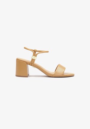 Beige hælsandal med firkantet tå, matte læderoverdel, en tynd ankelrem og en kraftig blokhæl. Guldfarvet aksesorie ved remmen.