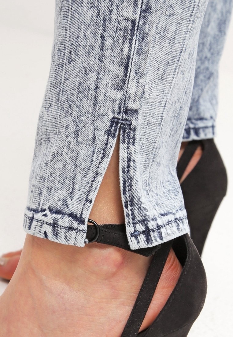 Jasnoniebieskie dżinsy z postrzępionym wykończeniem i rozcięciami na kostkach, w połączeniu z czarnymi sandałami na obcasie z paskiem na kostce.