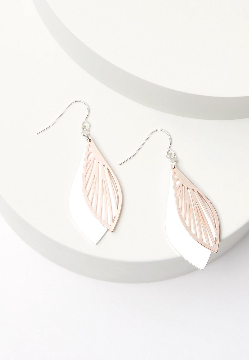Boucles d’oreilles pendantes en forme de feuille superposée en or rose et blanc avec crochets en argent sur une plateforme circulaire blanche.