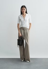 Άσπρο ριγωτό τοπ με κοντά μανίκια και κορδόνια μπροστά, μπεζ παντελόνι με φαρδιά μπατζάκια και ψηλή μέση με ζώνη, και μια μικρή μαύρη πλεκτή τσάντα.