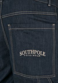 Jeans in denim scuro con tasca posteriore rinforzata. Logo "SOUTHPOL" ricamato in bianco. Cuciture a contrasto lungo i bordi delle tasche e le cuciture.