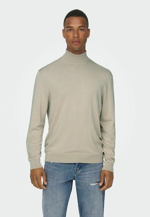 Suéter de cuello alto gris claro en una tela suave y texturizada, con mangas largas y un diseño ajustado. Combinado con jeans azules desgastados.