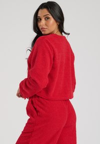 Rød, fuzzy loungewear-sæt bestående af en cropped top med lange ærmer og matchende højtaljede bukser. Tekstureret, blødt materiale.