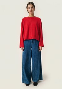 Rød kortærmet top med lange ærmer, parret med brede blå denimbukser. Glat stoftekstur med en afslappet pasform. Sorte sko fuldender looket.