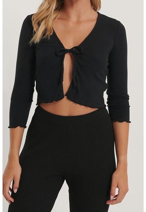 Mujer con un conjunto negro a rayas formado por dos piezas, que incluye un top de manga larga recortado con nudo en el pecho y pantalones de talle alto a juego.