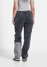Jeans neri a vita alta con una macchia grigia sbiadita su una gamba. Realizzati in denim con una vestibilità comoda. Presentano tasche posteriori e passanti per cintura.