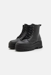 Bottes noires en cuir à cheville avec une semelle plateforme épaisse, bout rond, lacs sur le devant et accents en métal contrastants.