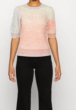 Personne portant un haut en maille à manches courtes pastel avec des dégradés de rose, orange et vert clair, associé à un pantalon noir.