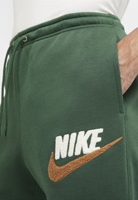 Πράσινα φούτερ παντελόνια Nike με ελαστική μέση, κορδόνι, πλαϊνές τσέπες και κεντητό λογότυπο σε άσπρο και καφέ. Μαλακή υφή υφάσματος.