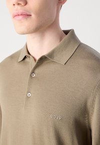 Olivenfarget polo-skjorte laget av teksturert stoff med krage, to knapper, og brodert "BOSS"-logo på venstre bryst.