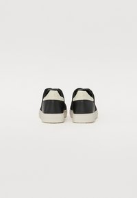 Sorte joggesko med hvite gummisalder; glatte lærpaneler ved hælen, teksturert stoff på sidene, og "CLAE"-merke på baksiden.