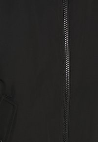 Giacca nera in tessuto liscio, con chiusura centrale a zip e tasche laterali. La texture appare elegante con dettagli minimi.