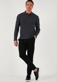Tricou polo cu mânecă lungă de culoare gri închis, realizat dintr-un tricot texturat, asortat cu pantaloni negri și adidași negri cu talpă albă și accente cu bretele.