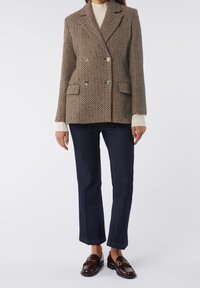 Femme portant un blazer croisé marron à motif, un pull crème, un jean bleu foncé à jambes droites et des mocassins marron foncé avec un détail doré.