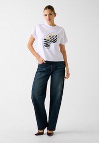 Wit katoenen T-shirt met een afbeelding van gestreepte zonnebrillen, gecombineerd met donkerblauwe wijde spijkerbroeken en puntige donkere schoenen.